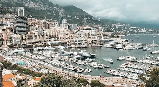 Monaco harbor with luxury yachts, high-rise buildings, and Mediterranean coastline against mountainous backdrop