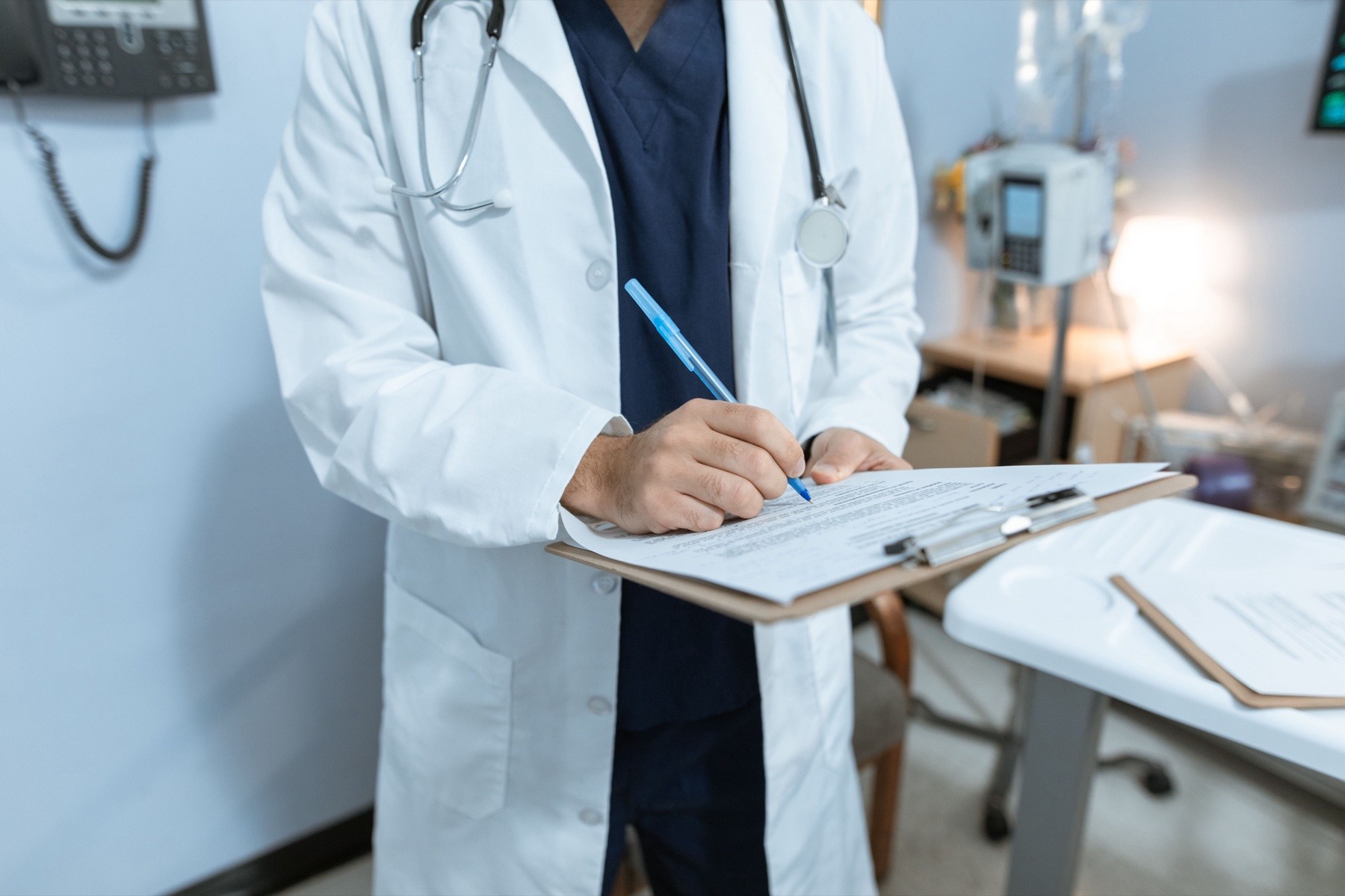 A doctor in a white coat writing notes on a clipboard in a treatment room, representing the medical record created after a dog bite